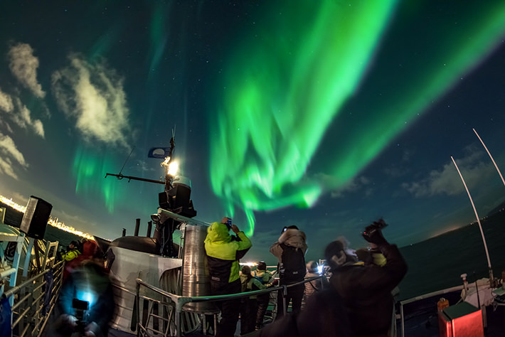 people on a boat photographing northern lights